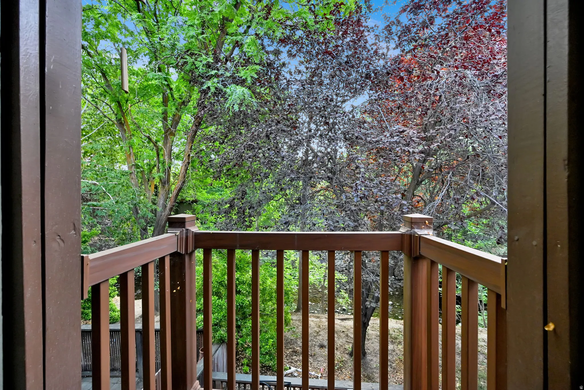Balcony with dark brown railings and balusters, overlooking varied mature trees