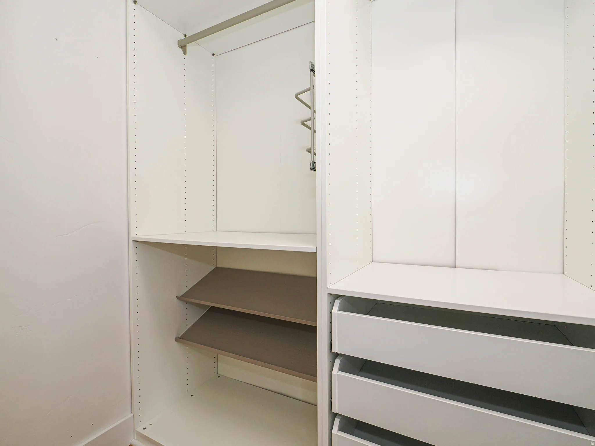 Built-in closet system featuring white shelving, a hanging rod, integrated drawers, and adjustable grey-toned shelves