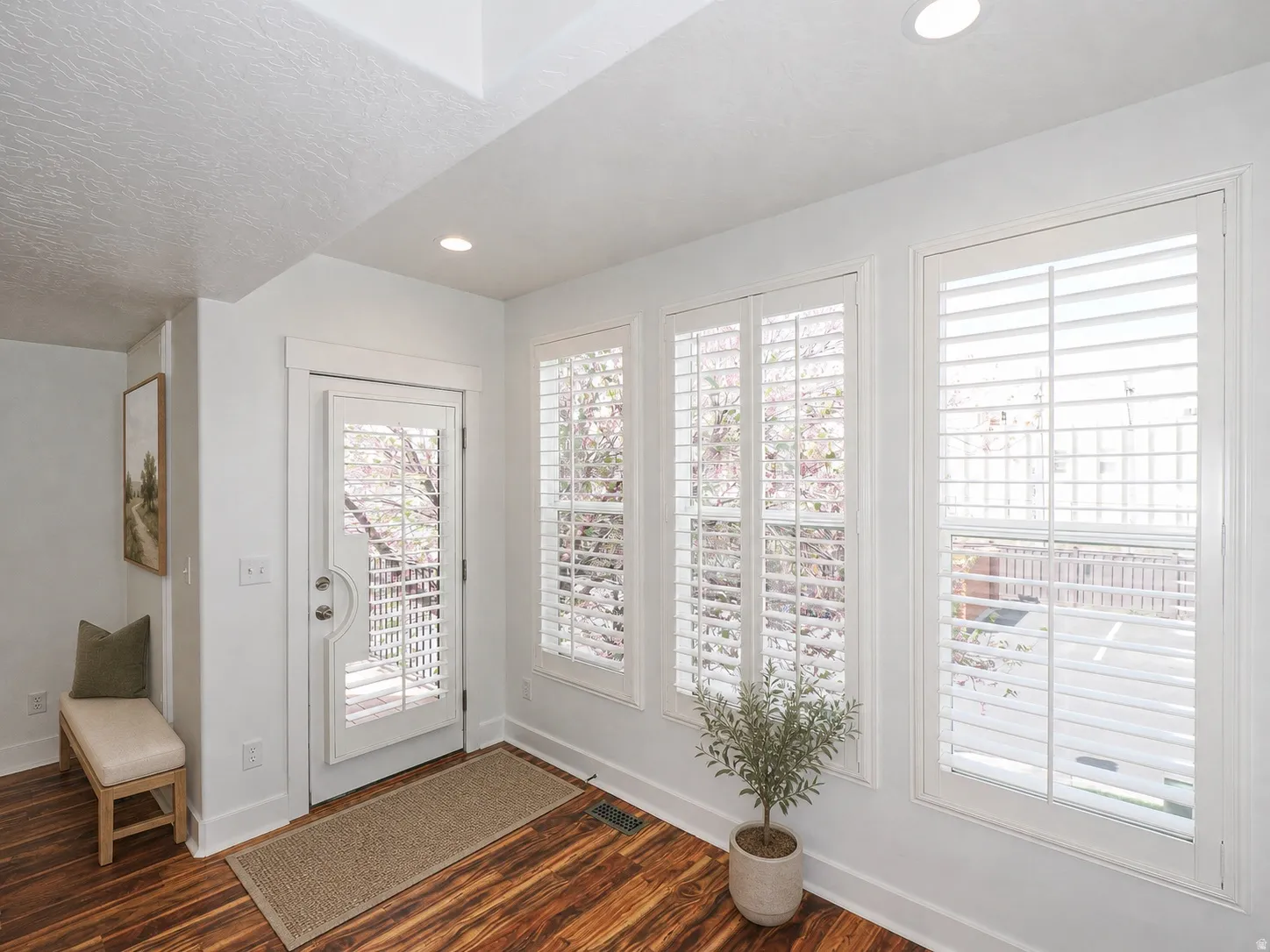 Entryway featuring rich wood-finish flooring, white plantation shutters, a glass-paneled door, recessed lighting, and white baseboards