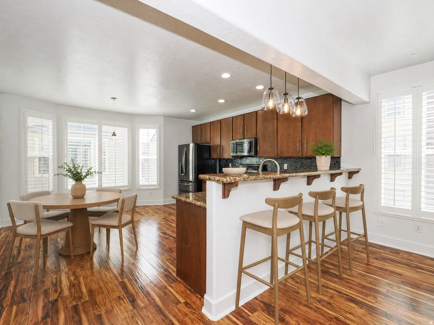 Open-concept kitchen and dining area featuring rich wood-finish flooring, dark wood cabinetry, a granite countertop with a breakfast bar, and stainless steel appliances