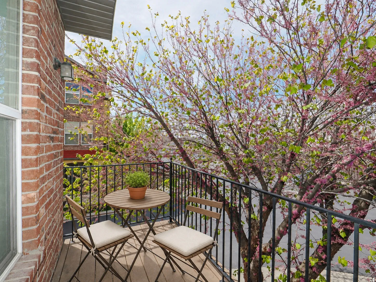 Private balcony featuring wood-finish flooring, a black metal railing, and a red brick exterior wall