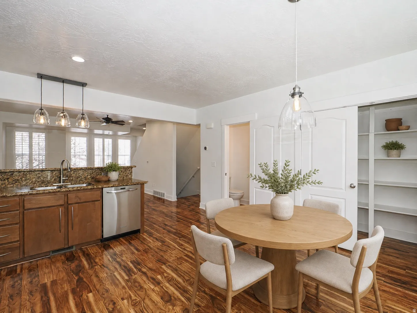 Open-concept kitchen and dining area featuring rich wood-finish flooring, a kitchen island with granite-style countertops, stainless steel appliances, and a contemporary pendant light fixture