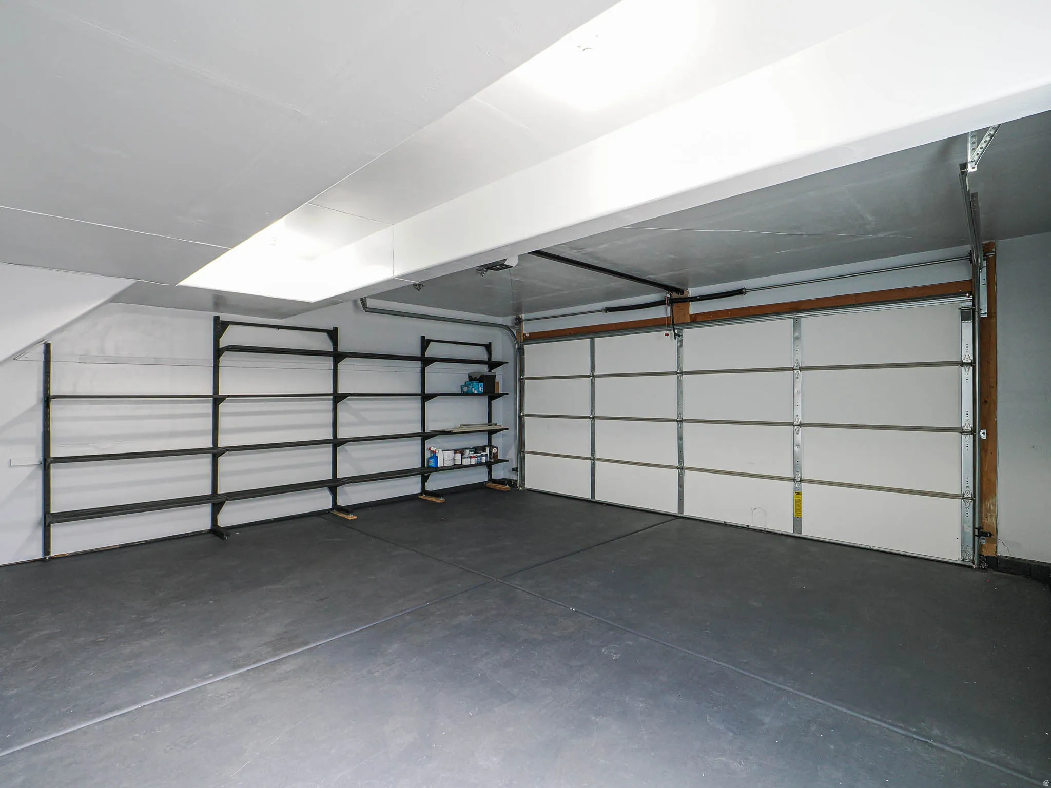 Spacious garage featuring a sectional overhead door, painted concrete flooring, built-in shelving, and overhead lighting