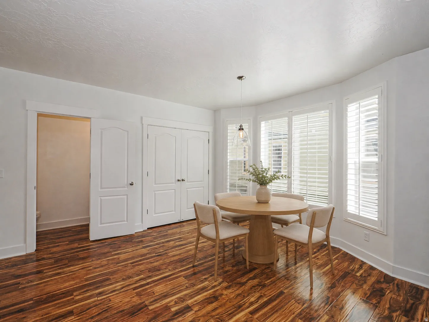 Bright room featuring rich wood-finish flooring, white trim, and a bay window with plantation shutters