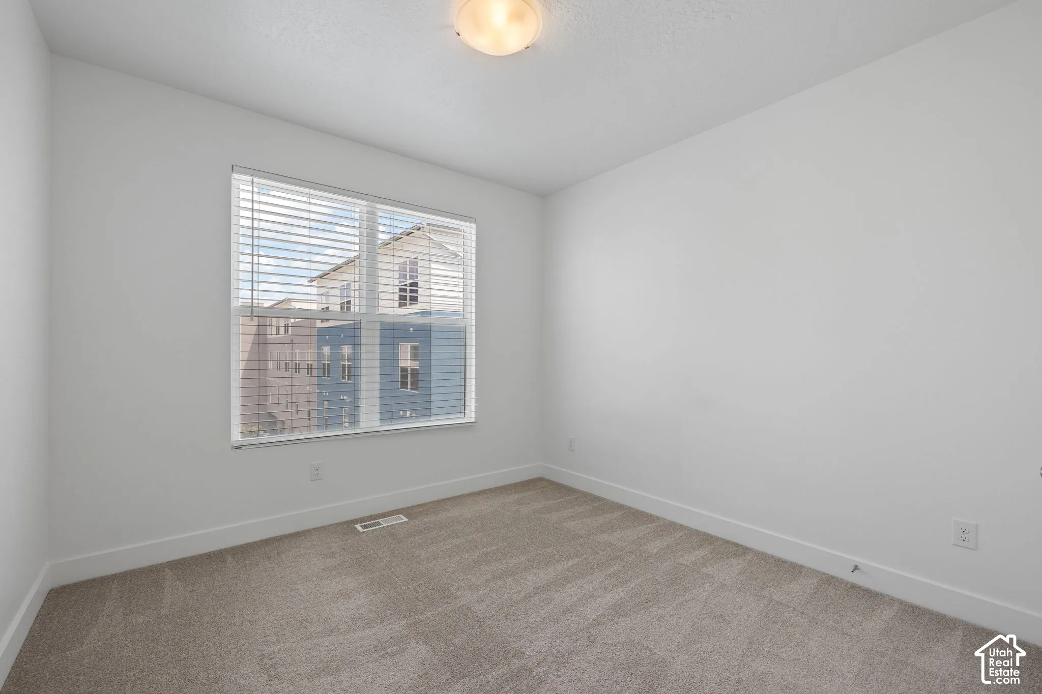 East facing bedroom featuring one large window with blinds, light-colored carpet, white walls, and white baseboards, abundant natural light