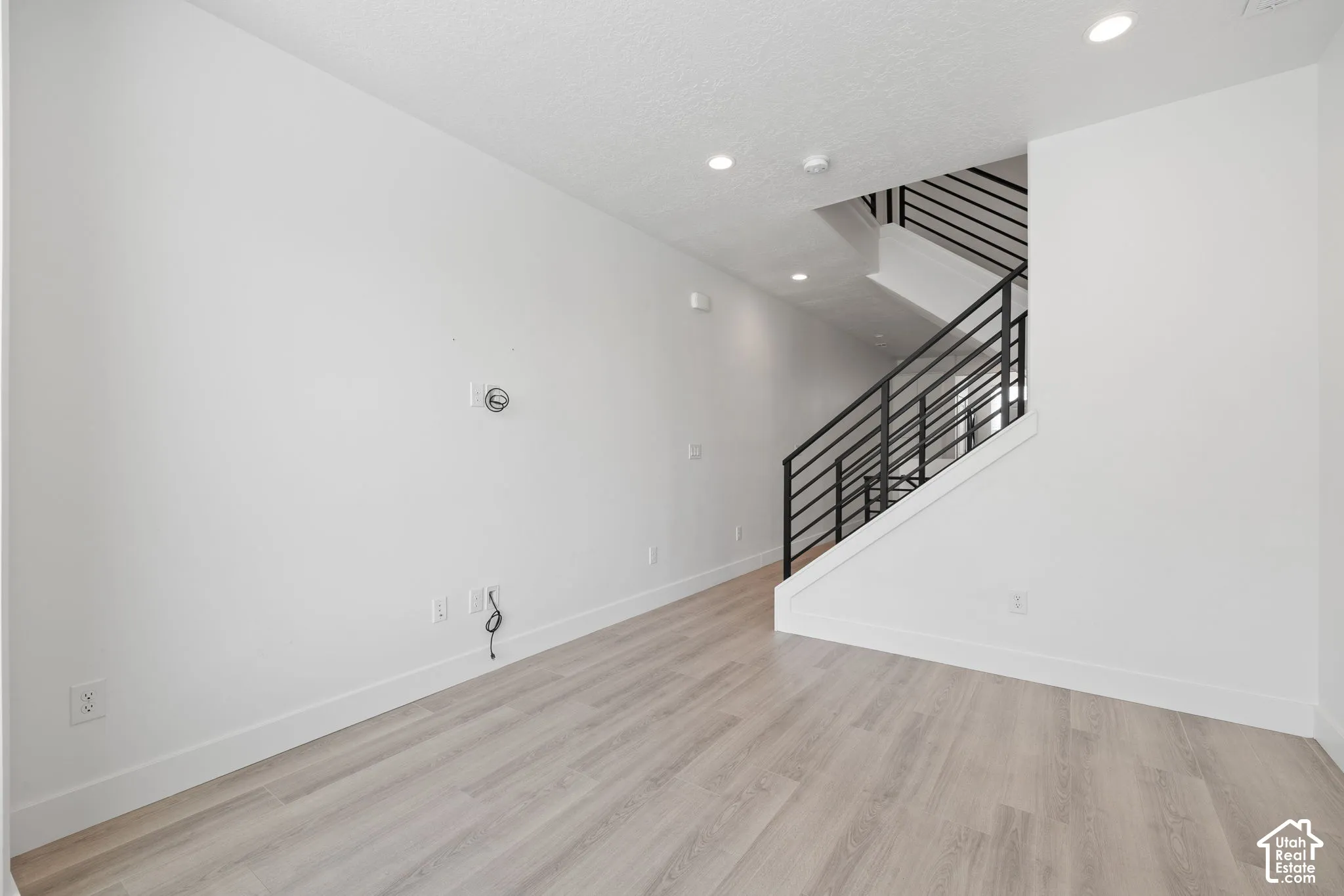 Open second floor living room featuring light wood-finish flooring, white walls, recessed lighting, and modern horizontal railing