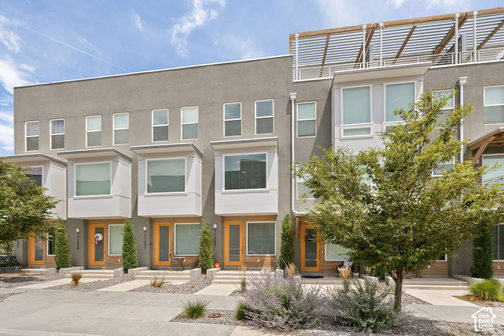 Contemporary multi-level townhome featuring a stucco exterior and wood-finish entry doors