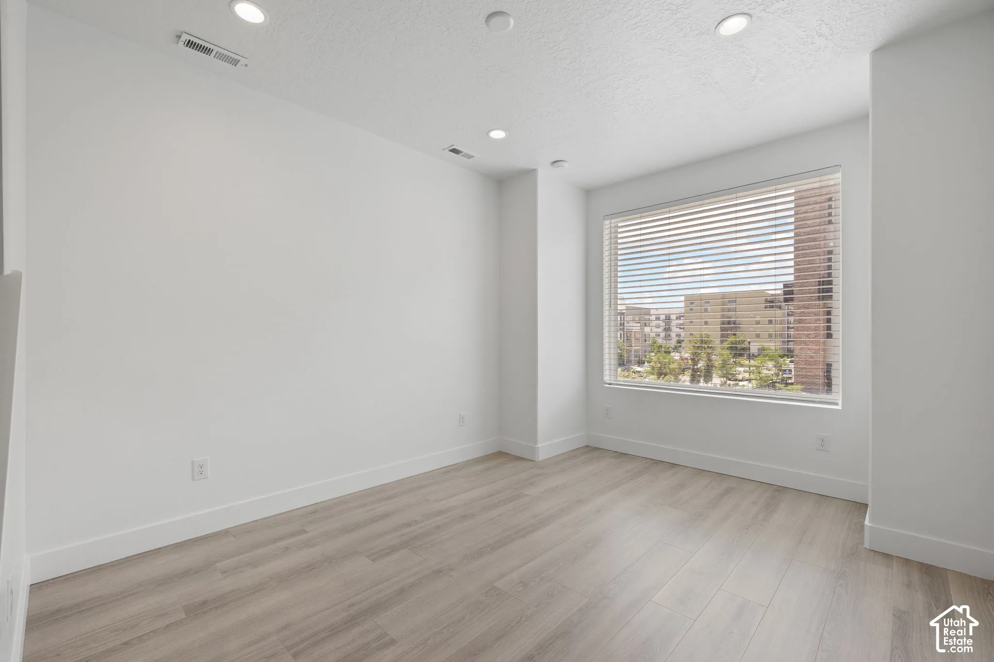 Second floor living room with wood-finish flooring, recessed lighting, and a large window with blinds featuring an urban view
