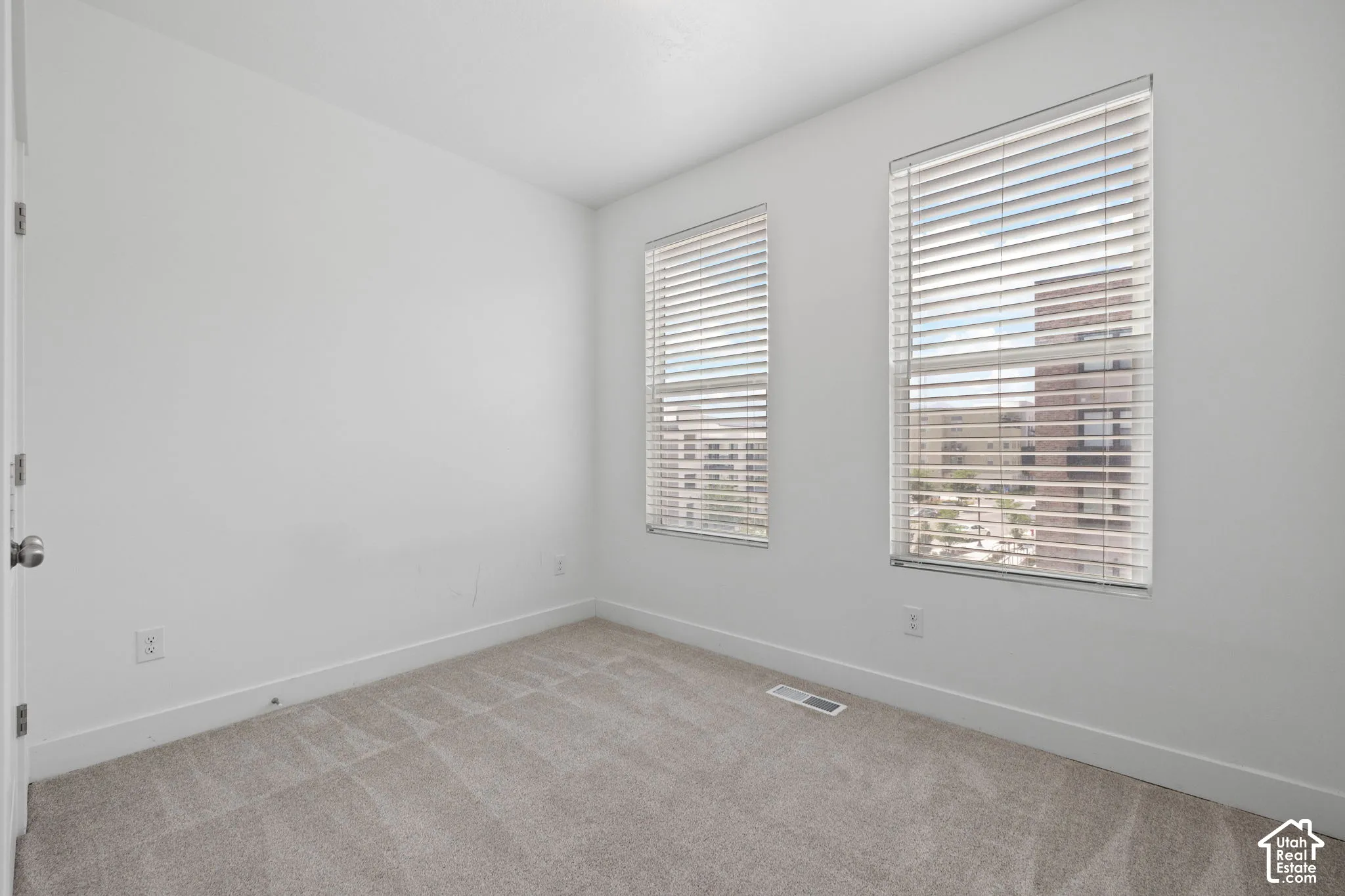 West facing bedroom featuring two windows with blinds, light-colored carpet, white walls, and white baseboards, abundant natural light