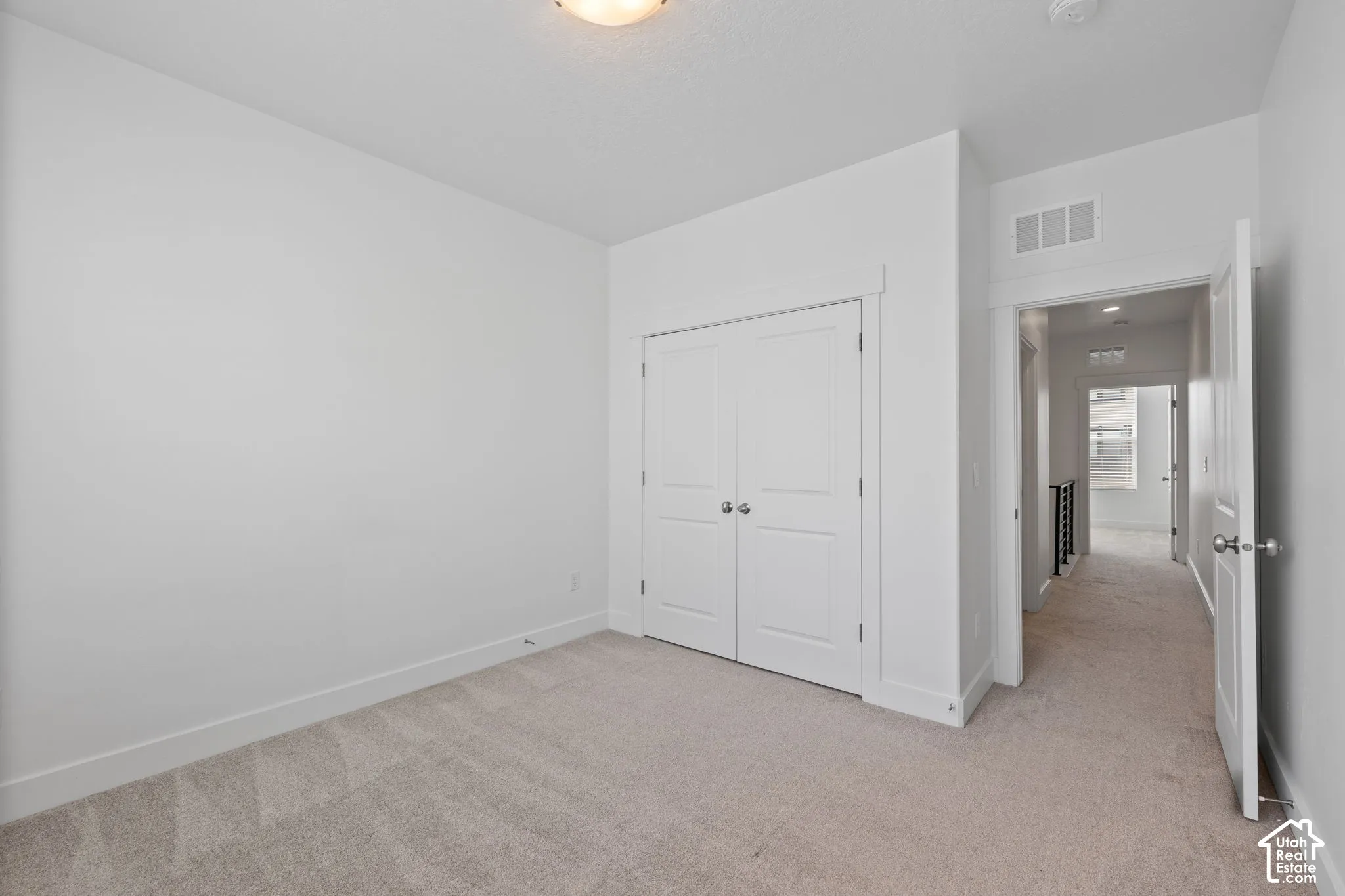 East facing bedroom featuring one large window with blinds, light-colored carpet, white walls, and white baseboards, abundant natural light