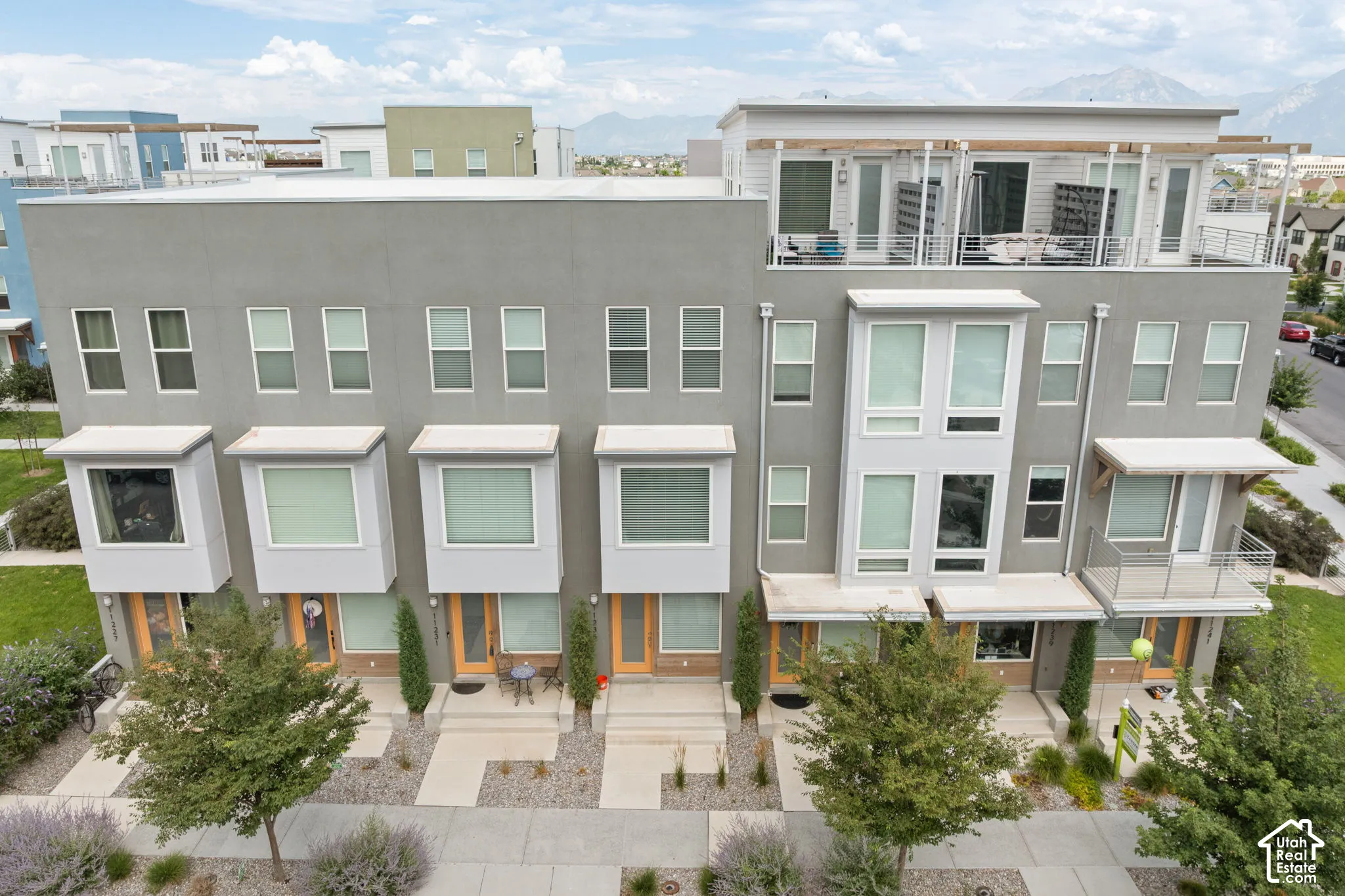 Modern townhome facade featuring a flat roofline, stucco exterior, bay windows, and private balconies