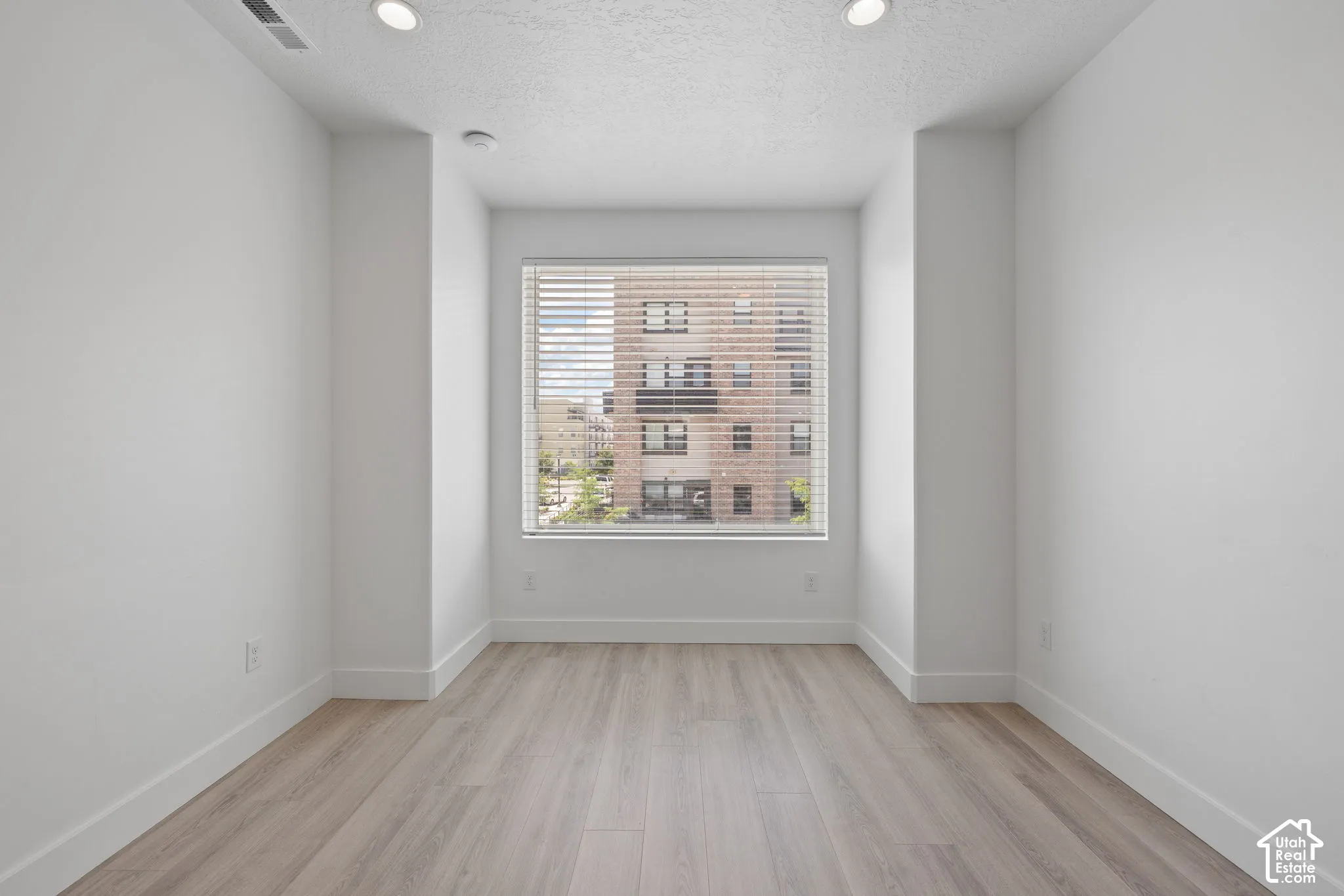 Second floor living room with wood-finish flooring, recessed lighting, and a large window with blinds featuring an urban view