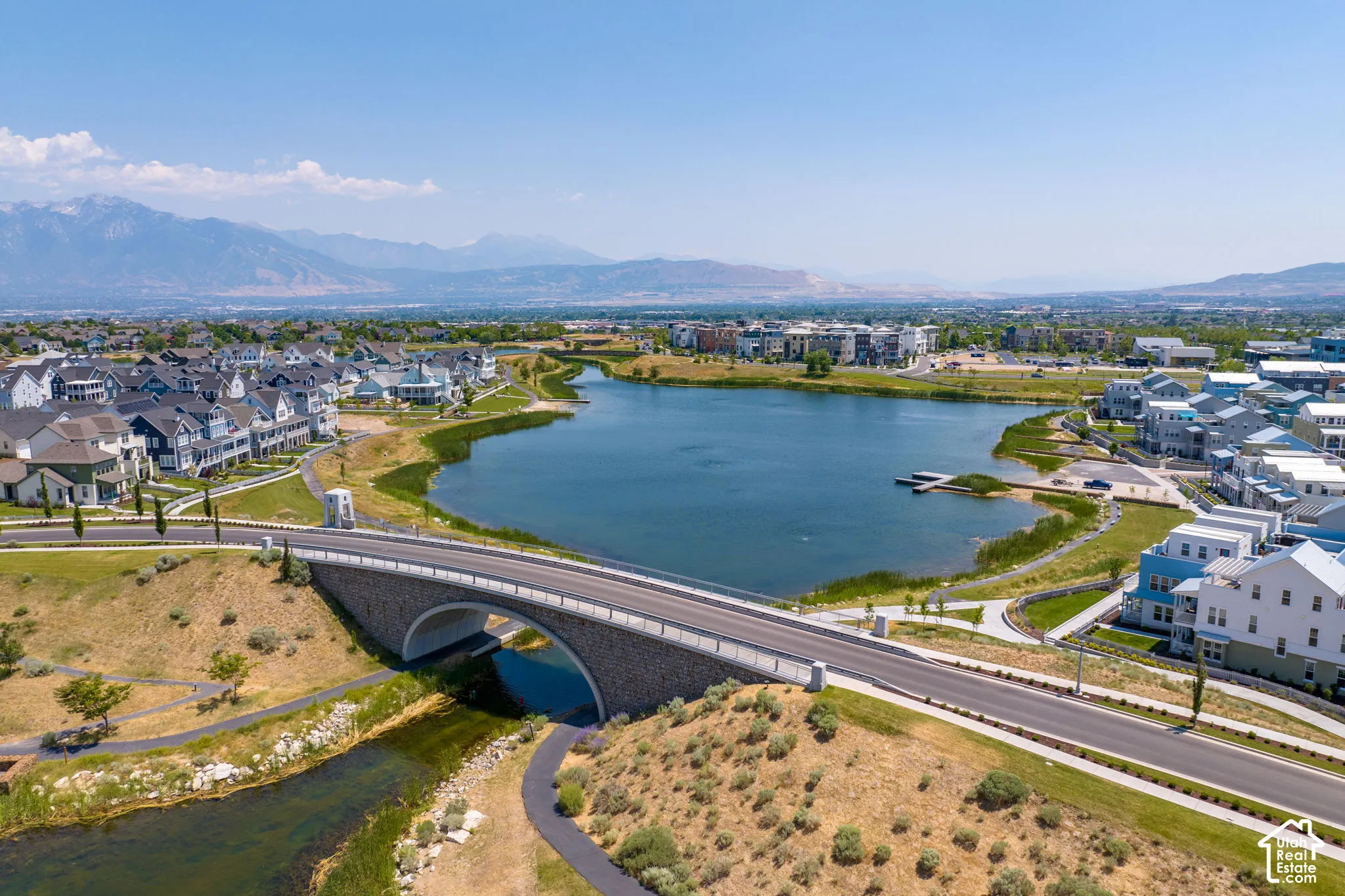 Expansive community featuring a large lake with docks, surrounding residential properties, a stone arch bridge, and paved pathways