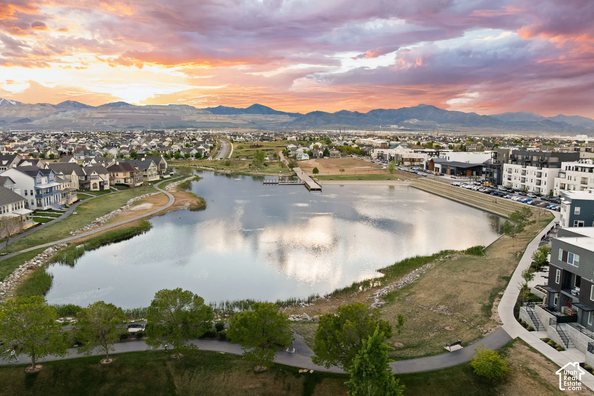 Expansive water feature with a pier, surrounded by a paved walking path and green spaces