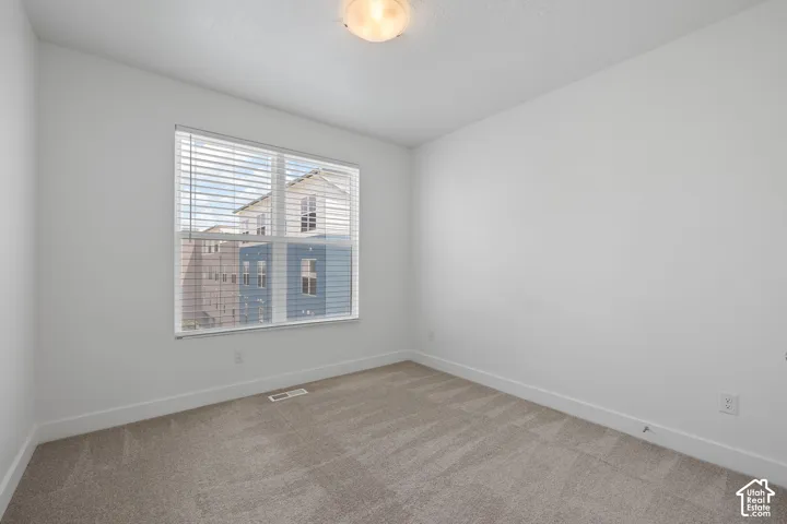 East facing bedroom featuring one large window with blinds, light-colored carpet, white walls, and white baseboards, abundant natural light