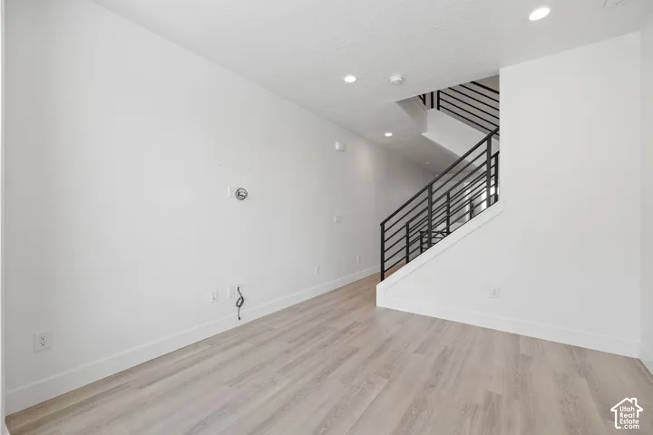 Open second floor living room featuring light wood-finish flooring, white walls, recessed lighting, and modern horizontal railing