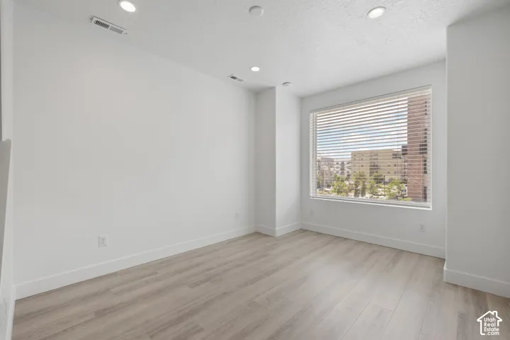 Second floor living room with wood-finish flooring, recessed lighting, and a large window with blinds featuring an urban view