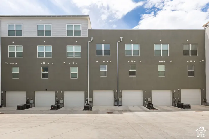 Multi-story building featuring a stucco exterior with multiple windows, individual garage doors, and an upper level with horizontal siding