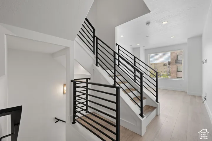 Modern staircase with black horizontal bar railings, light wood-finish treads, and white risers