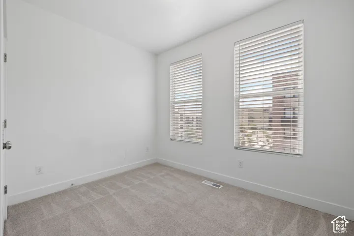 West facing bedroom featuring two windows with blinds, light-colored carpet, white walls, and white baseboards, abundant natural light