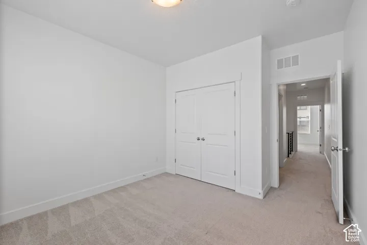 East facing bedroom featuring one large window with blinds, light-colored carpet, white walls, and white baseboards, abundant natural light