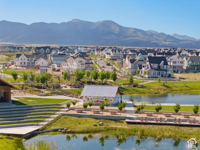 Expansive community featuring diverse architectural styles, a large pond, terraced seating, a waterfront recreational building, and mountain vistas