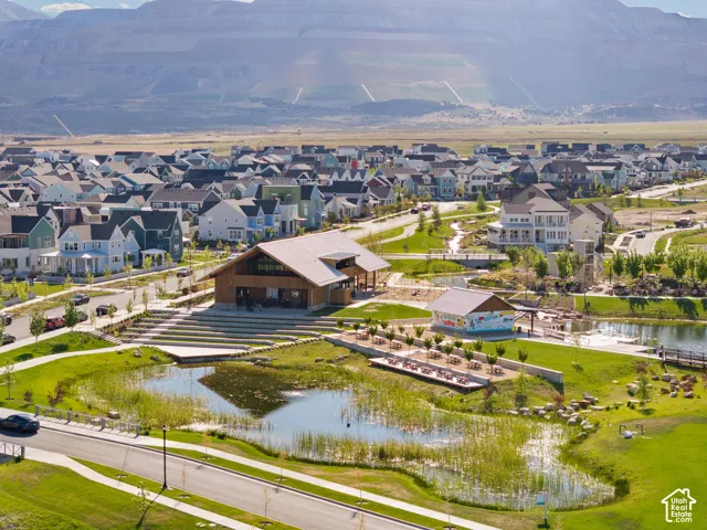 Aerial perspective showcasing a community with numerous residential properties, a central amenity building, and a prominent pond feature