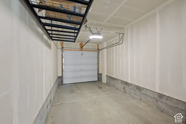 Garage with concrete flooring, overhead storage racks, garage door opener, and unfinished drywall walls