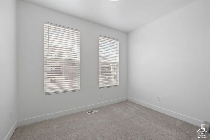 West facing bedroom featuring two windows with blinds, light-colored carpet, white walls, and white baseboards, abundant natural light