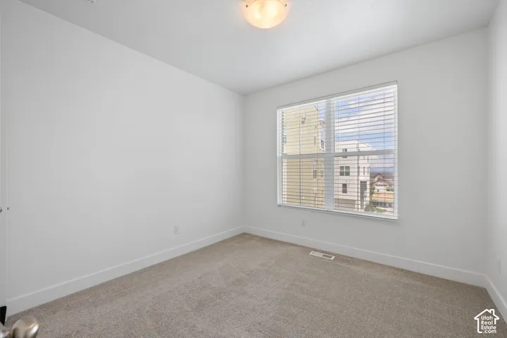East facing bedroom featuring one large window with blinds, light-colored carpet, white walls, and white baseboards, abundant natural light