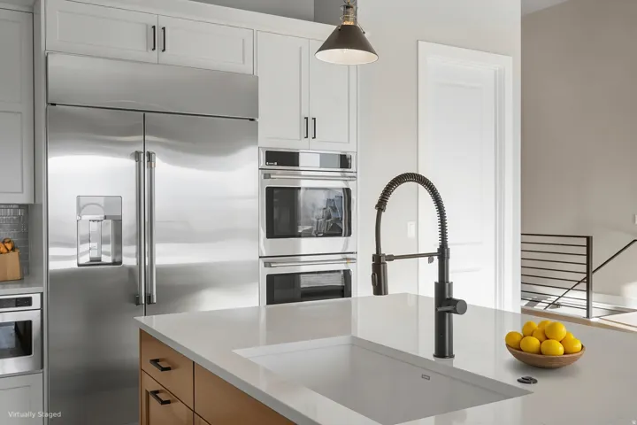 Gourmet kitchen with stainless steel appliances, built-in double ovens, white shaker cabinetry, and a center island with an undermount sink and matte black pull-down faucet