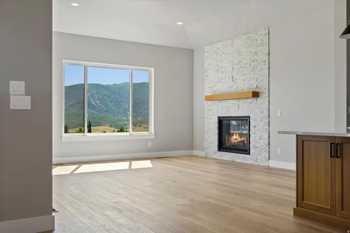 Spacious living area featuring light wood-finish flooring, a contemporary fireplace with a stacked stone facade and wood mantel, and large windows with a prominent mountainous landscape