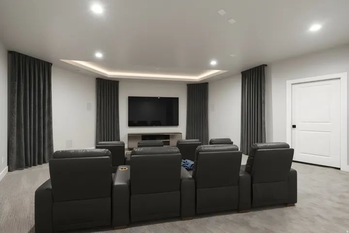 Home Theater Room featuring a tiered layout with four individual recliners, built-in ambient ceiling lighting with curved architectural detailing, wall-mounted flat-screen display, and dark charcoal curtains flanking the entertainment wall