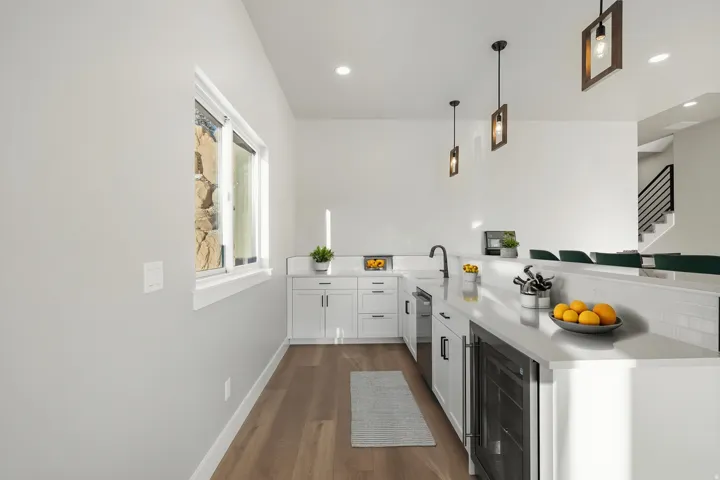 Galley kitchen featuring white cabinetry, stainless steel appliances, quartz countertops, subway tile backsplash, pendant lighting, and wood-finish flooring throughout