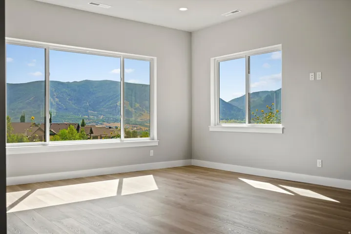 Bright, sun-filled room showcasing expansive multi-pane windows framing mountain scenery, wide-plank wood-finish flooring, neutral wall finishes, and abundant natural light throughout the space