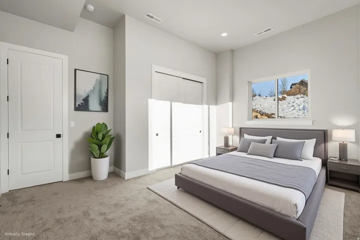 Bright primary bedroom showcasing recessed ceiling lighting, sliding glass doors with motorized window treatments, neutral carpeting, and a neutral color palette accented by framed artwork