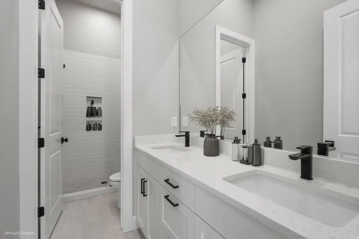 Modern primary bathroom featuring dual vanities with white quartz countertops, integrated rectangular vessel sinks, matte black hardware and faucetry, and a spacious walk-in shower with subway tile surround and frameless glass enclosure