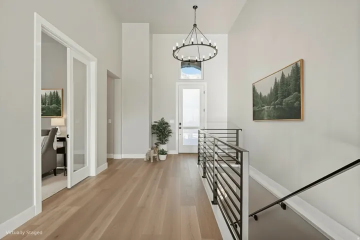 Bright hallway with wide-plank wood-finish flooring, crisp white trim and doors, and a modern metal railing
