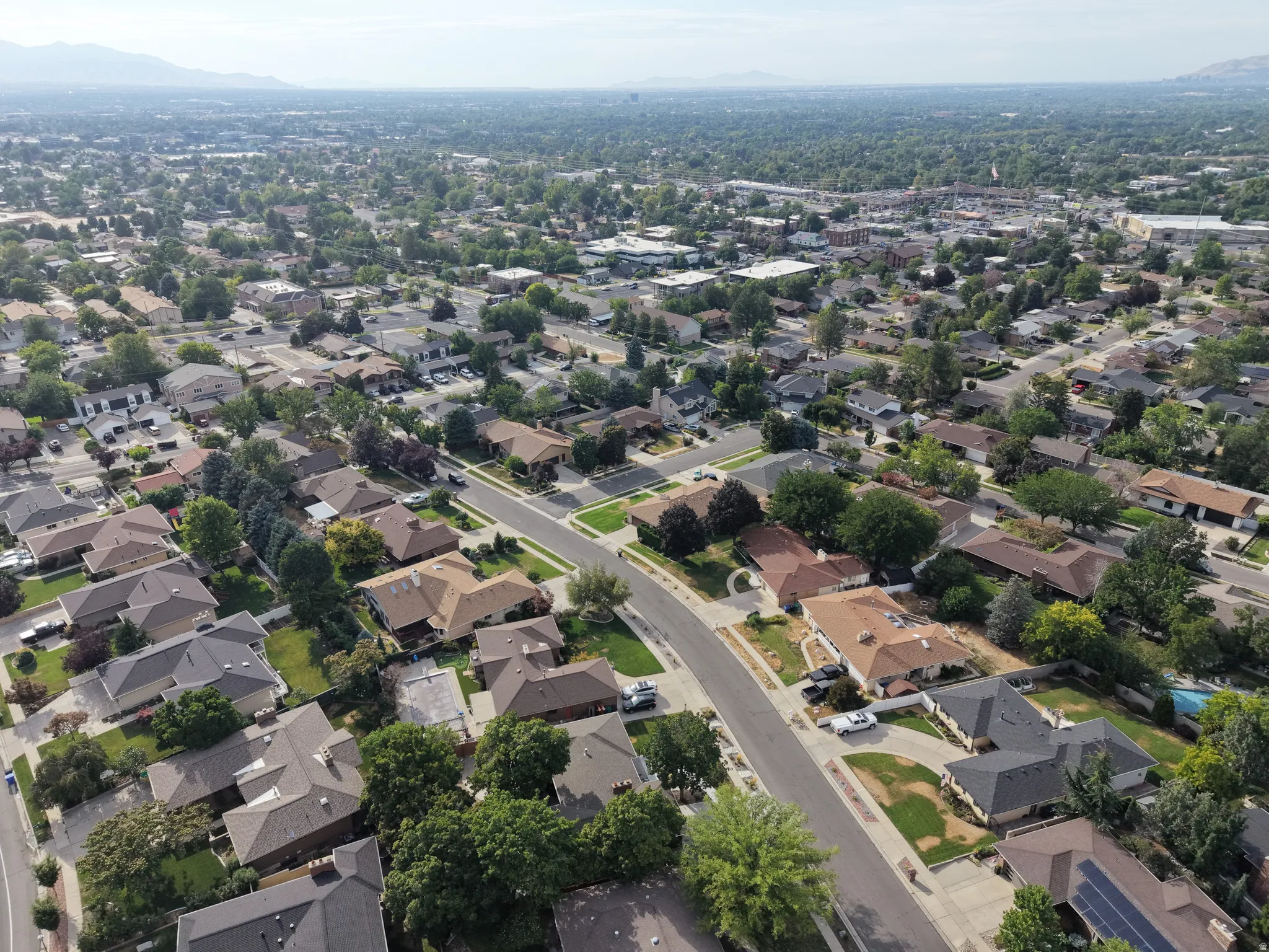 Aerial perspective showcasing a residential neighborhood with varied rooflines and established tree cover, set against a distant mountain range