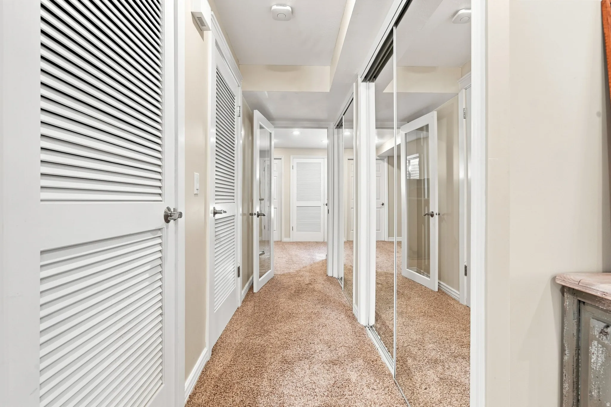 Hallway featuring light-toned carpeting, louvered doors, mirrored closet doors, and recessed lighting