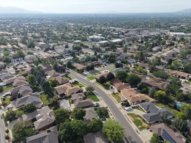 Aerial perspective showcasing a residential neighborhood with varied rooflines and established tree cover, set against a distant mountain range