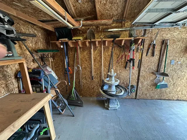 Garage space featuring oriented strand board walls, overhead lighting, and built-in tool storage