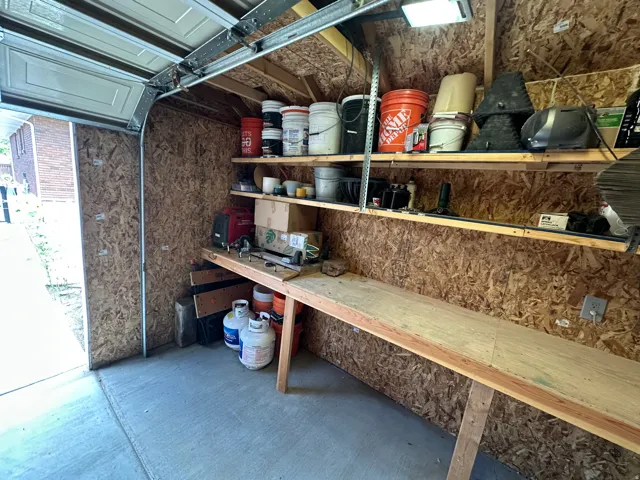 Garage interior featuring a concrete floor, exposed oriented strand board walls, built-in wooden shelving, and a built-in wooden workbench