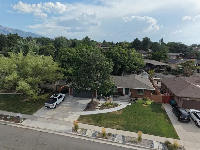 Brick ranch-style residence featuring a prominent front lawn, established landscaping, a concrete driveway, and an attached garage