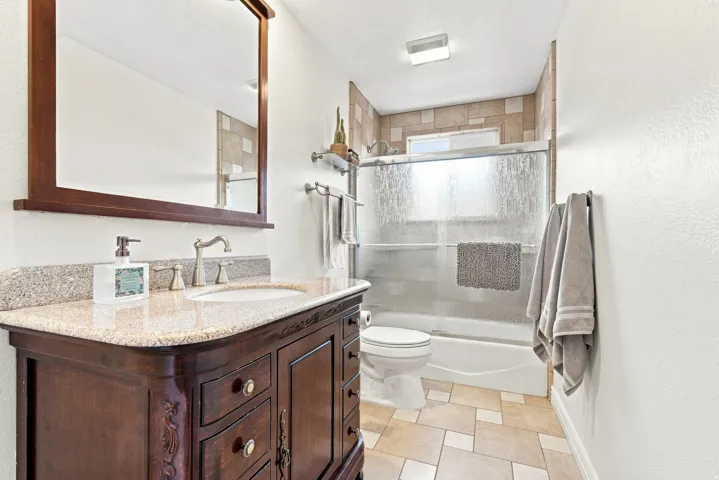 Bathroom featuring a wood vanity with a stone countertop, an undermount sink, and a framed mirror