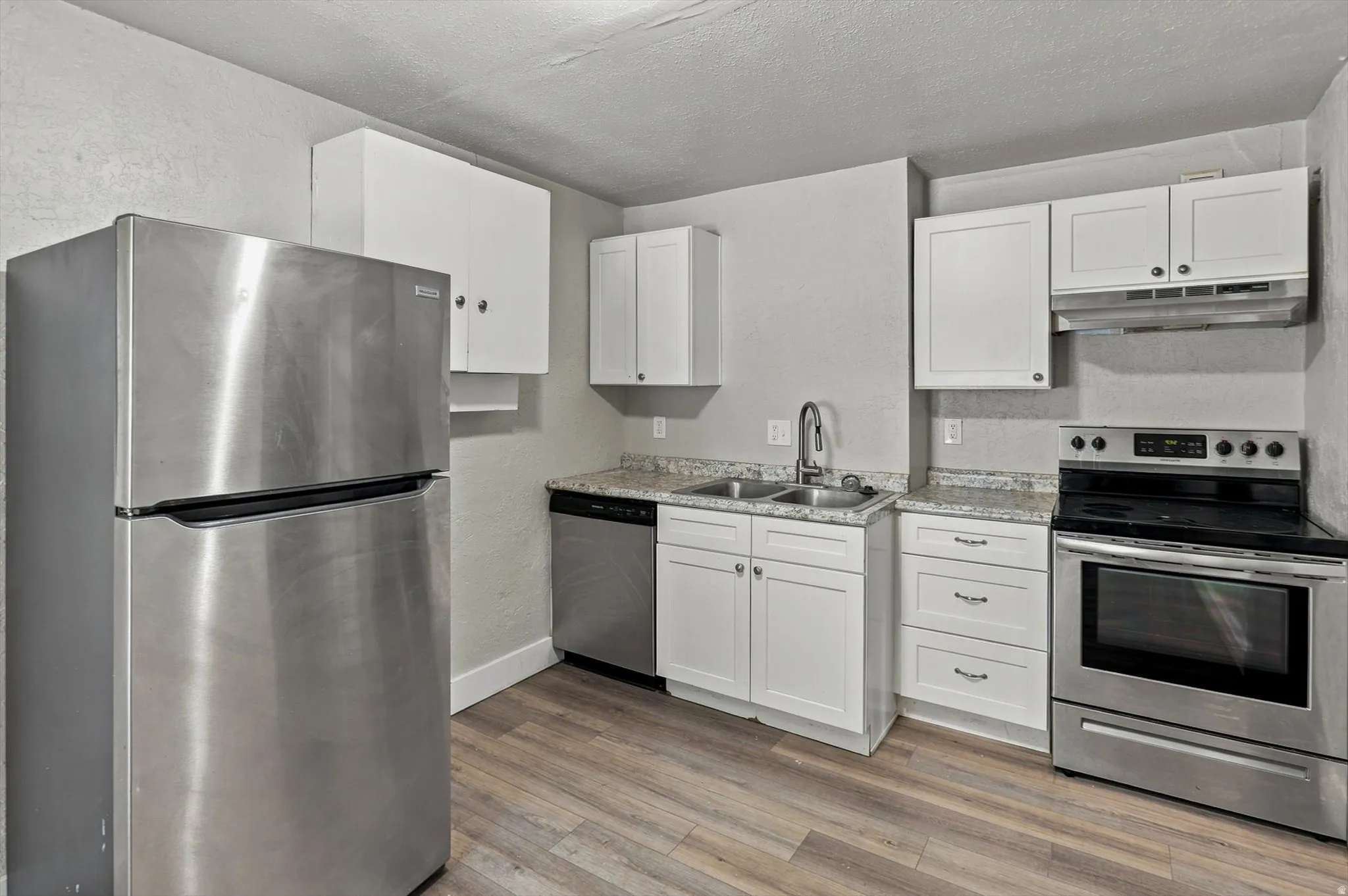 Kitchen featuring stainless steel appliances, white cabinetry, a double basin sink with a gooseneck faucet, light-toned countertops, and LVP flooring