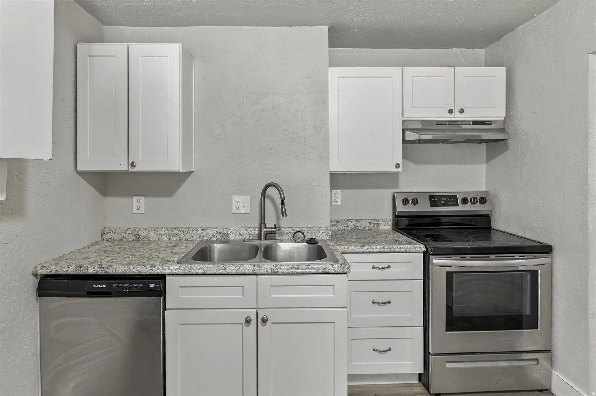 Kitchen featuring a double basin stainless steel sink, white shaker cabinetry, stainless steel dishwasher, stainless steel range, and light countertops