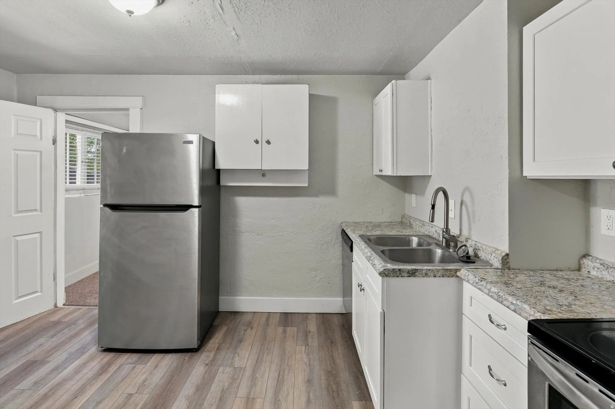 Kitchen featuring LVP flooring, white cabinetry, a double basin stainless steel sink with gooseneck faucet, light-colored countertops, and a stainless steel refrigerator