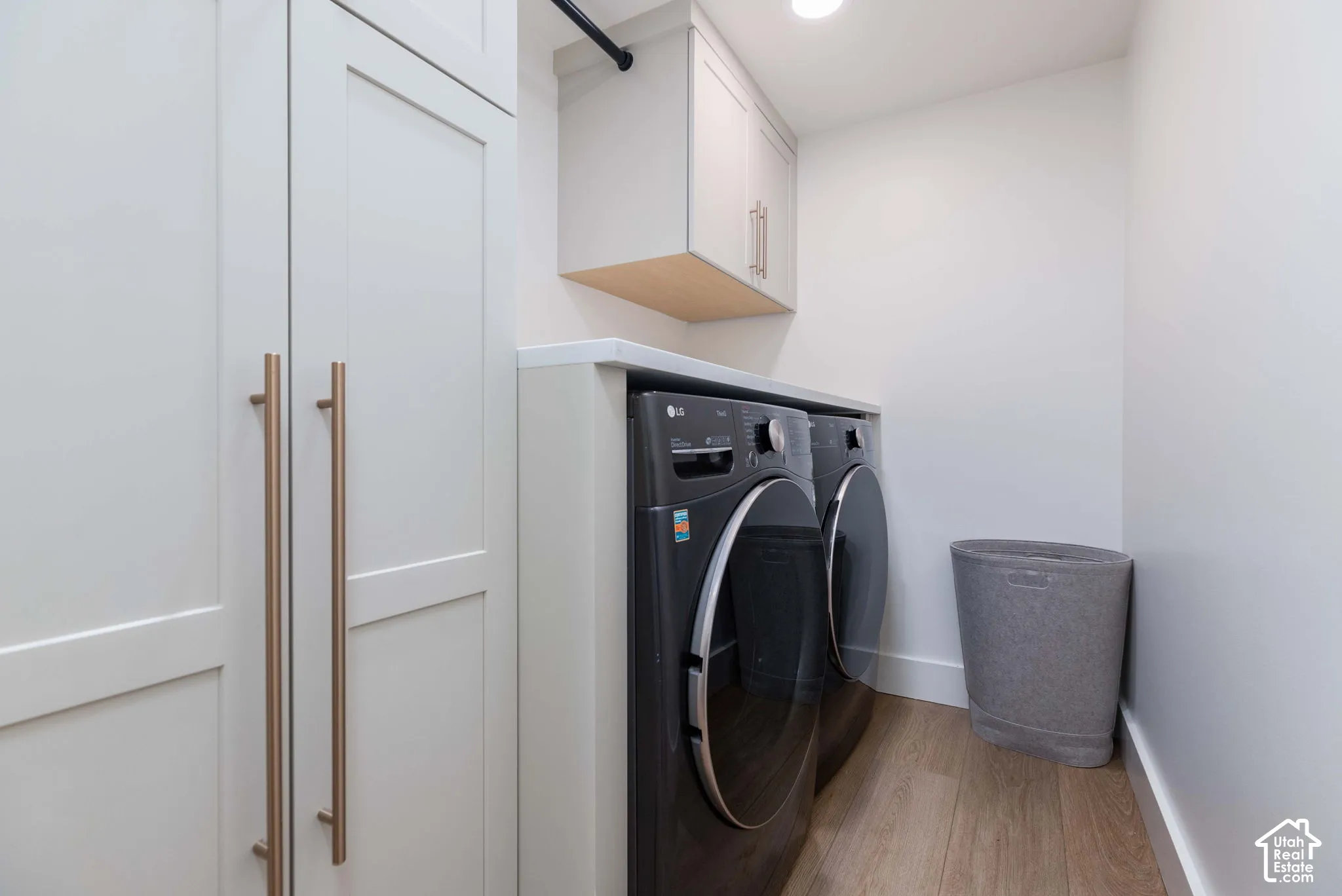 Dedicated laundry area featuring a white countertop, light wood-finish flooring, and shaker-style cabinetry with long metallic pulls