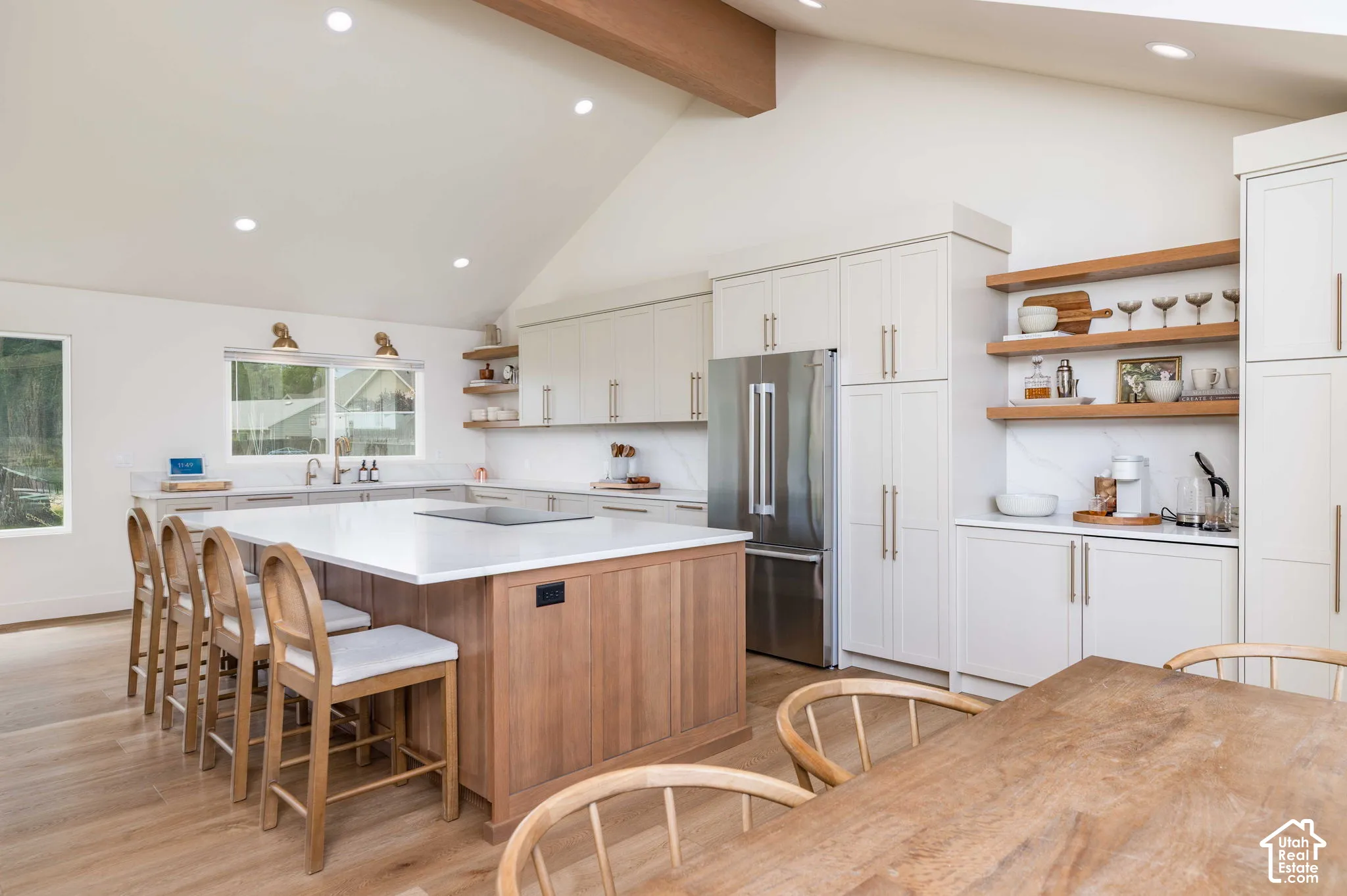 Kitchen featuring an expansive island with a white countertop, light wood-finish cabinetry, integrated stainless-steel appliances, open shelving, and recessed lighting